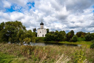 Kar beyazı, eski kilise yaz fırtınasından önce yeşil bir çayır ve gölün arka planında.