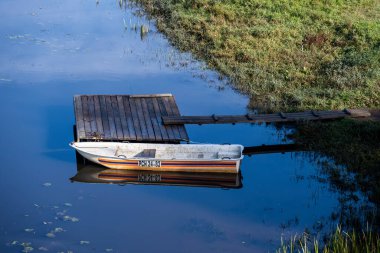 Mavi nehirdeki ahşap iskelede beyaz bir tekne.