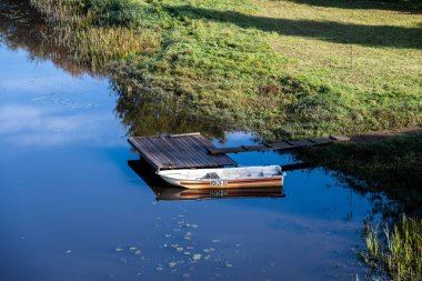 Mavi nehirdeki ahşap iskelede beyaz bir tekne.