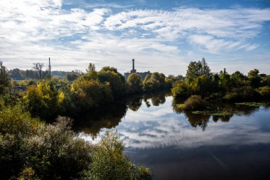 Sahilde yeşil ağaçları olan mavi nehir ve sudaki bulutların yansımaları.