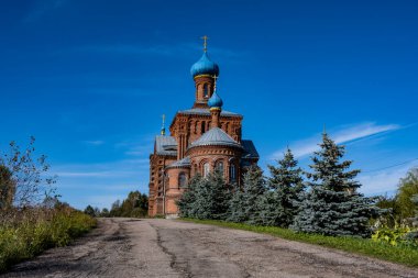 Ormanın yakınındaki bir tepede mavi gökyüzüne karşı eski bir kırmızı tuğla kilise.
