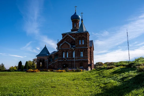 an old red brick church on a hillock near the forest against a blue sky