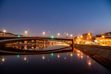 Şafak vakti büyük bir metropolün nehir kenarına parlayan fenerlerin yansımasıyla.
