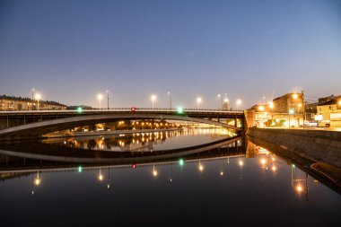 Şafak vakti büyük bir metropolün nehir kenarına parlayan fenerlerin yansımasıyla.