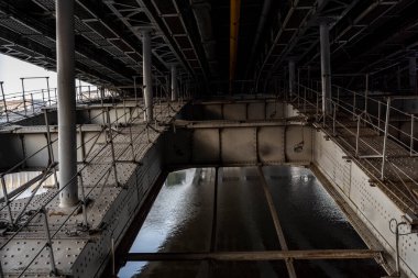 Gündoğumunda nehrin karşı kıyısında metal perçinlenmiş levha tabanlı klasik yol köprüsü.