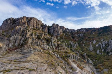 Gökyüzünün arka planında sıradışı çıkıntıları ve hikayeleri olan güzel dağlar ve bir drondan çekilen vadi.