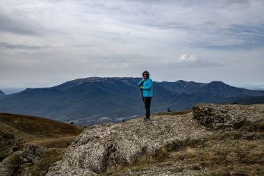 Dağın tepesinde mavi ceketli kadın turist yüzen bulut seviyesinde.