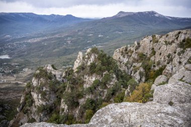 Dağların ve vadinin panoramik manzarasına karşı yeşil çam ağaçları ve sonbahar gökyüzü