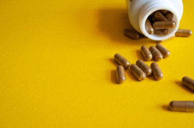 Sarı arka planda hap şişesinden dökülen haplar..