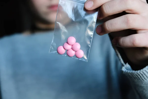 Onu tutan kadın küçük bir plastik torba fermuar pembe hap ver. Uyuşturucu, medecine, gri bir arka plan üzerinde narcotik.