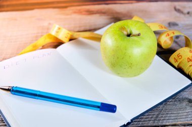 Bir diyet planlama. Bir not defteri c bir yazıt - diyet, bir ölçüm bandı, bir elma ve kalem, portre.