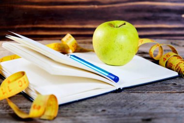 Boş açık defter ile yeşil elma ve sarı santimetre beğenmezlerse kalem. Konsept spor, diyet, fitness, sağlıklı yeme.