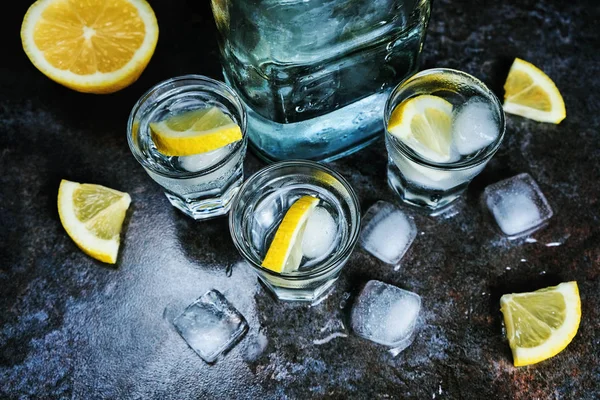 Vodka. Tiros, copos com vodka e limão com gelo. Fundo de pedra escura . — Fotografia de Stock