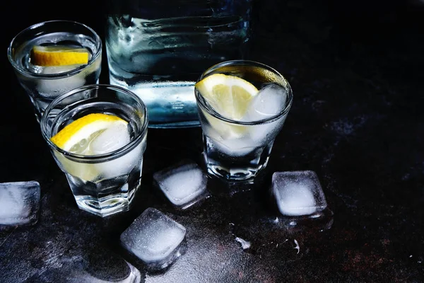 Vodka. Tiros, copos com vodka e limão com gelo. Fundo de pedra escura . — Fotografia de Stock