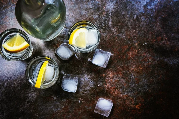 Cold vodka in shot glasses with lemon on stone background. Top view, copy space. — Stock Photo, Image