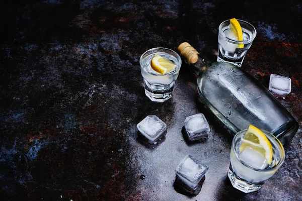 Kalter Wodka in Schnapsgläsern mit Zitrone auf Steinhintergrund. Ansicht von oben, Kopierraum. Stockbild