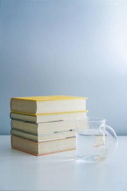 Bir yığın kitap ve beyaz masanın üzerinde bir bardak su.