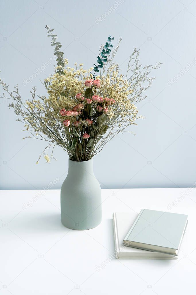 Vase and book notebook with dried flowers on the white desk
