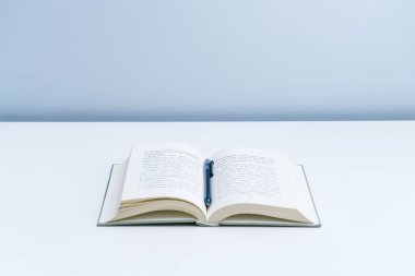 Açık bir kitap beyaz bir masanın üzerine lambayla konur. Düzenlenmiş bir yığın kitap ve beyaz bir masada şeffaf bir bardak.