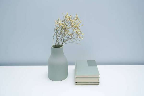 Vase and book notebook with dried flowers on the white desk