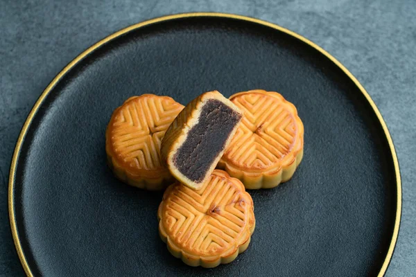 Moon cakes for the Mid-Autumn Festival are placed on a black plate with gold trim