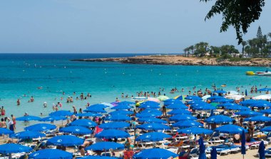 PROTARAS, CYPRUS - 16 Haziran 2018 'de Kıbrıs Rum Kesimi' nin Protaras kentinde güneşli bir günde yerel belediye plajı insanlarla dolup taşıyor. 