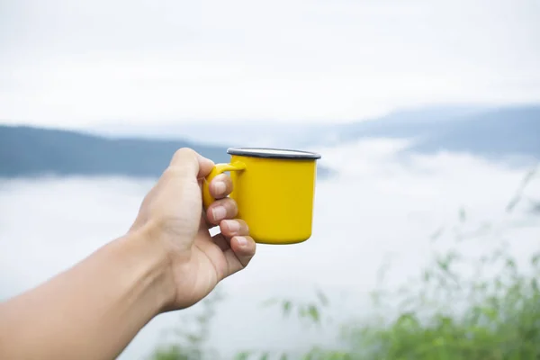 Hand holding yellow mug with nature background