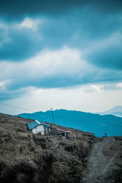 Small house on hill against sky with clouds