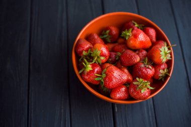 Yakın plan olgun, lezzetli çilekler, portakal kâse tabağında, ahşap masa arkasında. Antioksidan besin, sağlıklı organik gıda konsepti. Kopyalama. Düz yatıyordu. Gün ışığı