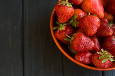Yakın plan olgun, lezzetli çilekler, portakal kâse tabağında, ahşap masa arkasında. Antioksidan besin, sağlıklı organik gıda konsepti. Kopyalama. Düz yatıyordu. Gün ışığı