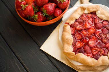 Fırınlanmış çilekli turta ve ahşap arka planda taze çilek dolu turuncu tabak. Lezzetli geleneksel ev yapımı turta. Ev işi. Kopyalama. Düz yatıyordu. Gün ışığı