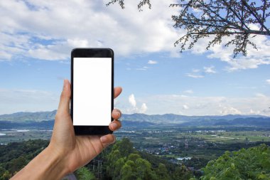 Siyah smartphone ile beyaz perde için sahte bulut ve mavi arka plan ile dağın zirvesinde tutan el.