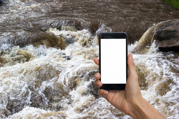 Hand holding black smartphone with white screen for mock up on sudden flood water wave as background.