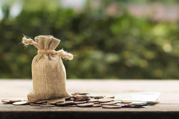 Saving money for future, home, car, education, investment, descendants concept : Money bag with many coins on wood table with green nature as background. Copy space for your text.
