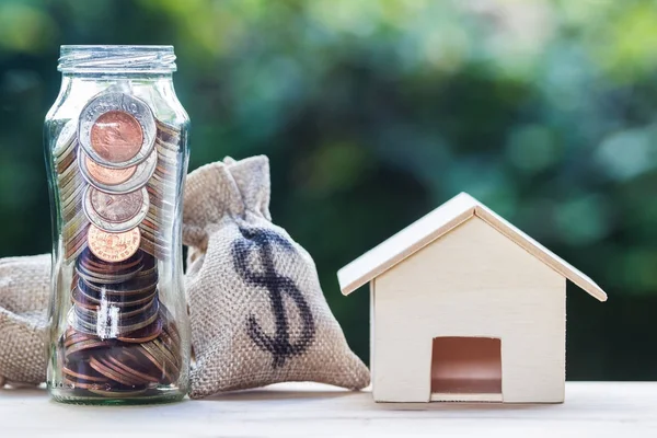 Home loan, mortgages, property investment, savings money concept : US dollar in a money bag and jar, small residential, house model on table  with nature background. Exchange of finances and houses.