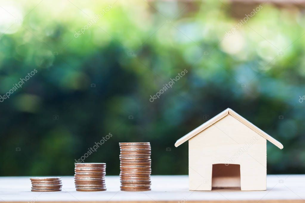 Property investment,  home loan, house mortgage, resident financial concept : Stacking coins in 1 to 3 step with small house on table over green nature background. Demonstrate growth of real estate.