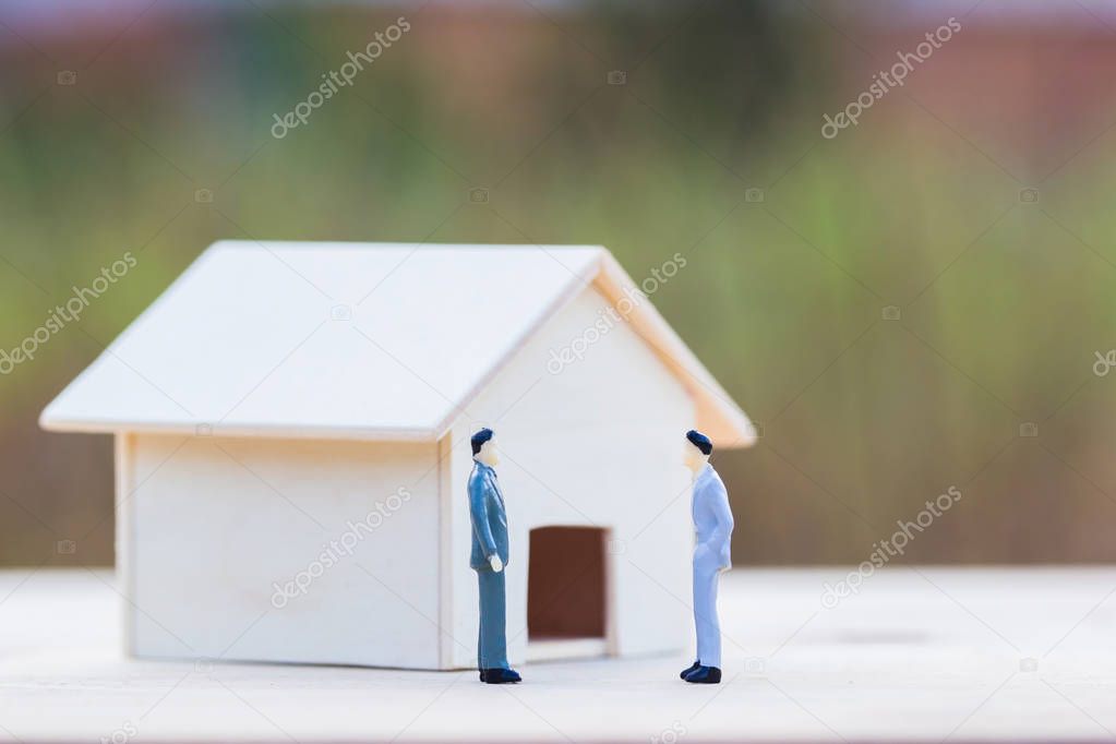 Home bargain, real estate, loan, house lender reverse mortgage concept : Two Miniature businessmen bargain front small residence on wooden table and blurred green nature as background. Trading house