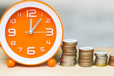 Money savings, Investment, growing concept : Stacking growing higher coins respectively and orange clock on wooden table with copy space. Saves money for the future. Time investment use money for work clipart