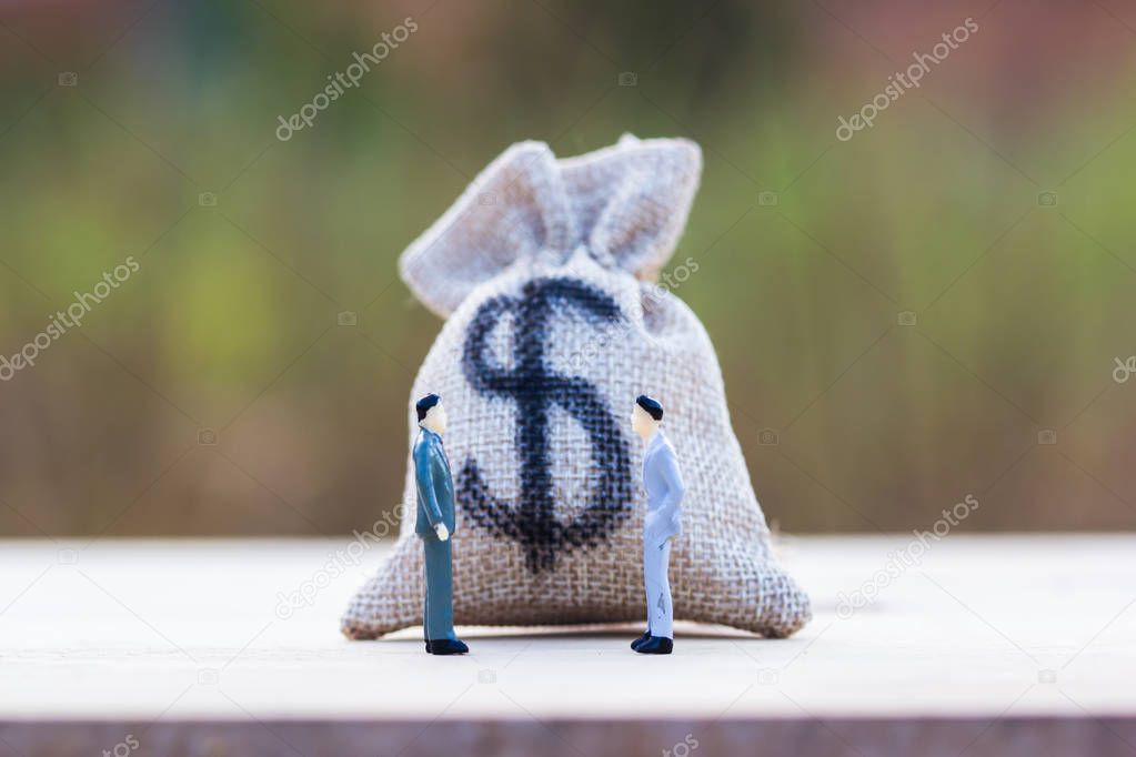 Financial investment negotiation,discussion among CEO or execute level concept: Money bag on wooden table with Miniature figurine two businessmen talk on money invest contract agreement.