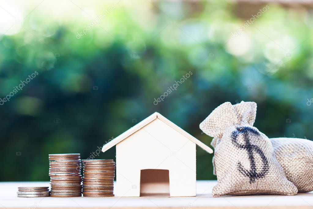 Home loan, mortgages, debt, savings money for home buying concept : US dollar in a money bag, small residential, house model on table against green nature background. Exchange of finances and houses.
