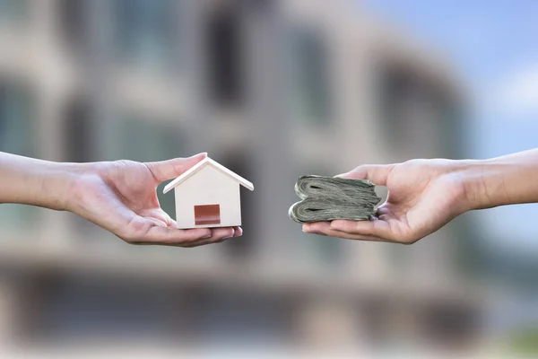 Home loan, mortgages, debt, home buying concept. Hand holding small resident exchange money on blurred real estate background. Exchange of finances and houses.