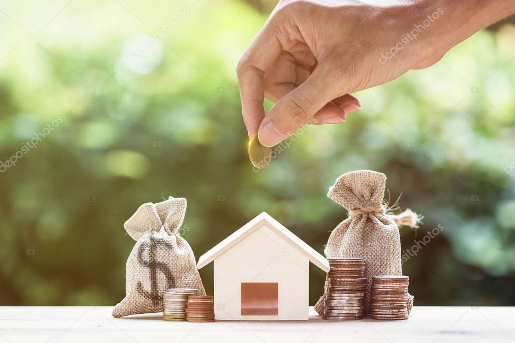 Saving money, home loan, mortgage, a property investment for future concept. A man hand putting money coin over small residence house and money bag with nature background. A sustainable investment.