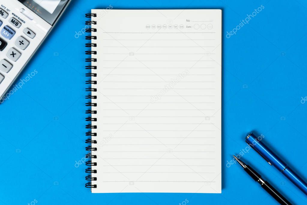 Open notebook with calculator and pen from top view on blue back