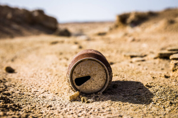 Пустая банка содовой, лежащая в песке пустыни с холмами сзади.