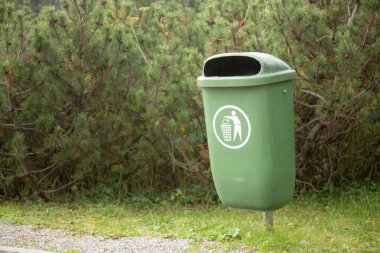 Kozalaklı ağaçların önündeki çöp tenekesi