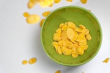 Masanın üzerinde sarı mısır gevreği olan yeşil kase.