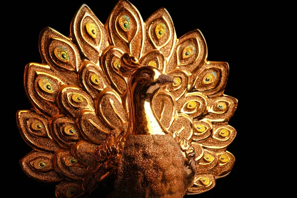 Altın tavus kuşu heykeli koyu arkaplanda izole.