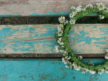Beyaz çiçekli yonca çelengi, turkuaz ahşap arka planda.              