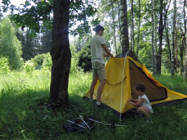 Baba ve oğul ağaçların arasına sarı bir turist çadırı kurdular..         
