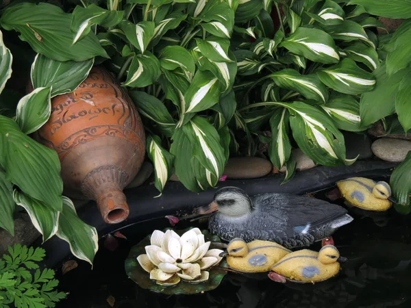 Garden decor - a pond with ceramic ducks and an old clay bottle, against a background of green beautiful leaves